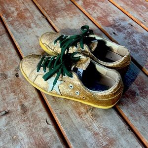Gold Golden Goose sneakers with green laces.
